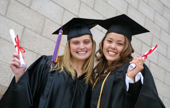 Two female graduates smiling with diplomas